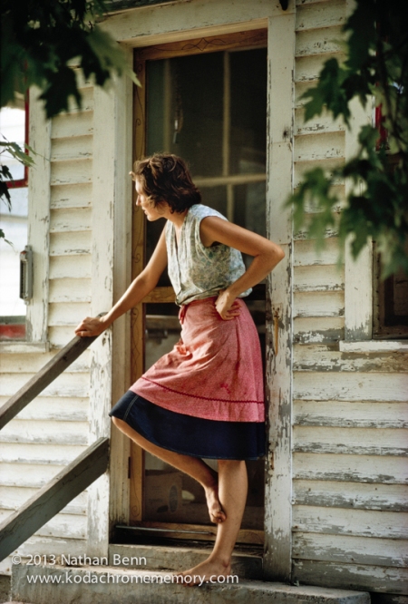 Young farmwoman waiting at the kitchen door at Lorien Farm in New Haven, Vermont. The young woman shows an uncommon natural beauty and grace as she waits at the door to the house on a warm New England summer day. The farm uses muscle and horsepower rather than tractors. 1973.